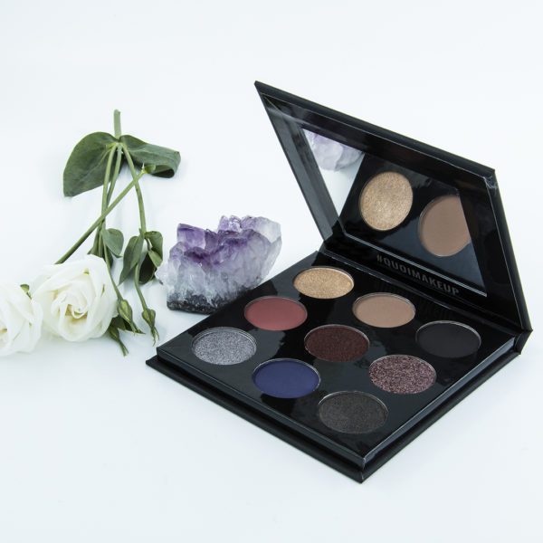 eyeshadow palette next to white roses and amethyst crystal