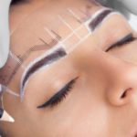 Permanent make-up for eyebrows of beautiful woman with thick brows in beauty salon. Closeup beautician doing  tattooing eyebrow.